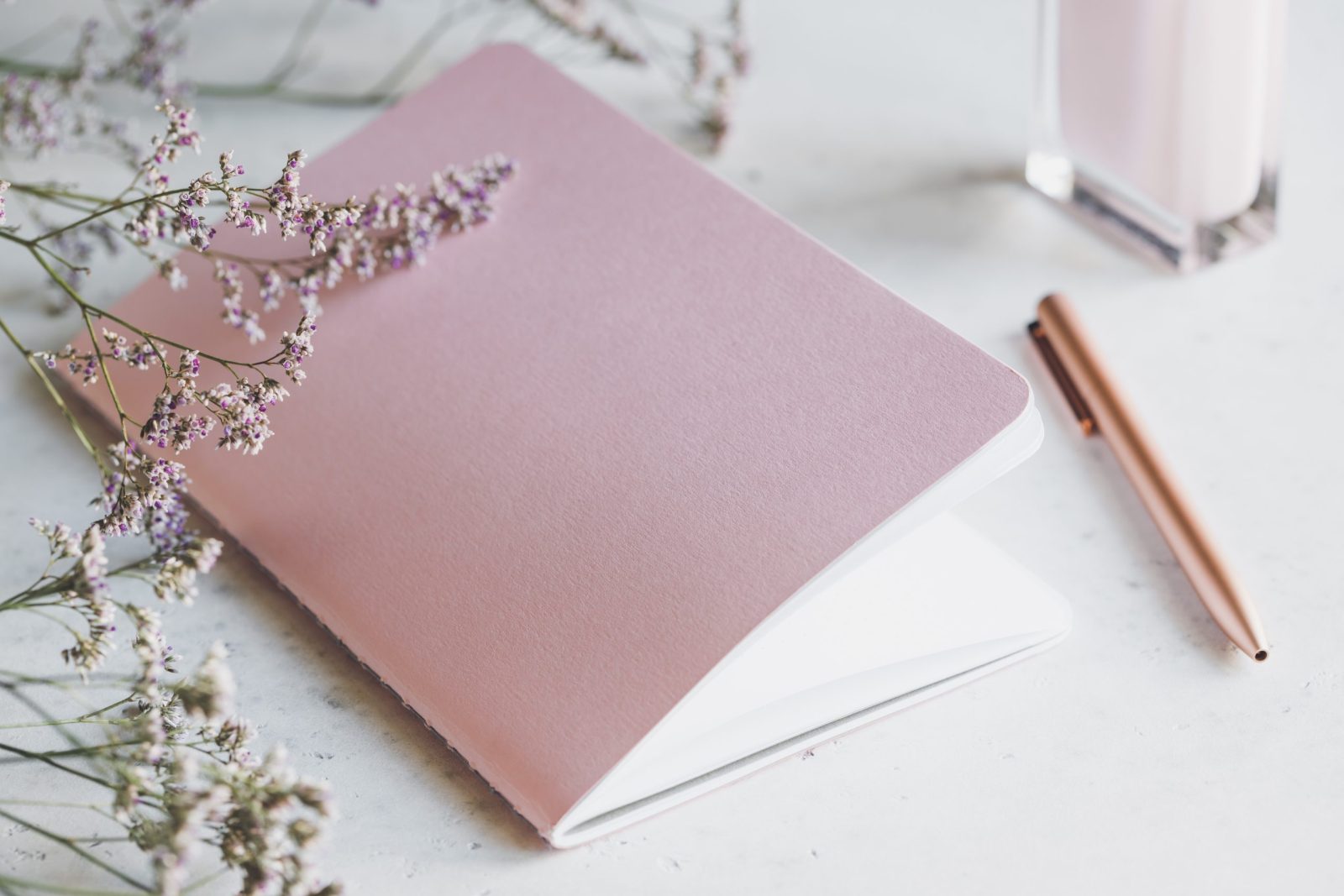 Bienfaits de la sophrologie : carnet rose et stylo posés sur une table claire, près d'un bouquet de fleurs séchées